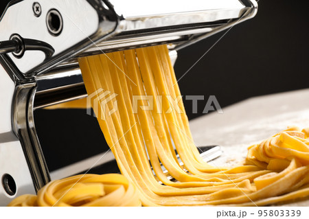 Pasta maker machine with dough on table against black background, closeup Pasta maker machine with dough on table against black background, closeup 95803339
