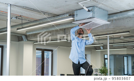 Caucasian bearded man repairing the air conditioner in the office.  95803607