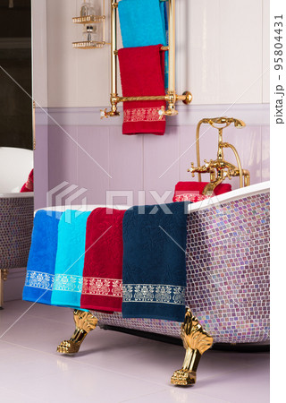 A vertical shot of colorful bamboo towels hanging on a mosaic purple bathtub in a bathroom 95804431