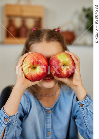 Happy emotional little girl holding red an apple in hands covering eyes at home Happy emotional little girl holding red an apple in hands covering eyes at home 95804583