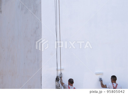 Unrecognizable painters painting the wall in white on scaffolding Unrecognizable painters painting the wall in white on scaffolding 95805042