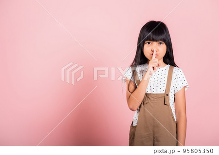 Asian kid 10 years old holding finger on lips symbol of hush gesture of asking quiet Asian kid 10 years old holding finger on lips symbol of hush gesture of asking quiet 95805350