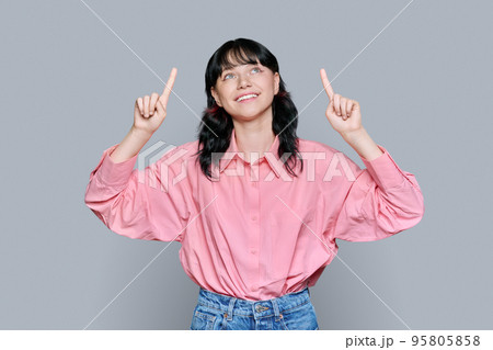 Young woman pointing fingers up, space for copyspace text, on grey background 95805858