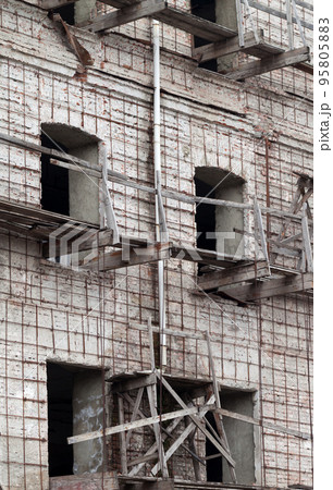 Brick wall of old destroyed house without windows with wooden broken scaffold Brick wall of old destroyed house without windows with wooden broken scaffold 95805883