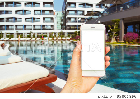 Mobile phone in hand near swimming pool for lifestyle design. Smartphone mockup white screen. Modern lifestyle. Modern technology device screen. Summer vacation. 95805896