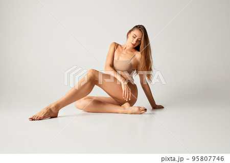 Portrait of beautiful woman with slim figure posing in underwear isolated over grey background. Moisturizing body 95807746