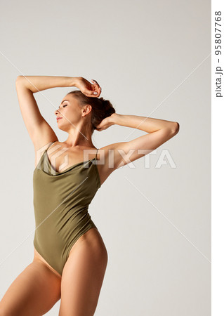 Portrait of beautiful woman posing in green bodysuit over grey background. Perfect body shape Portrait of beautiful woman posing in green bodysuit over grey background. Perfect body shape 95807768