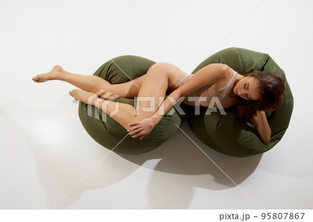Portrait of beautiful slim woman in beige underwear posing on floor pillows isolated on white background. Top view 95807867