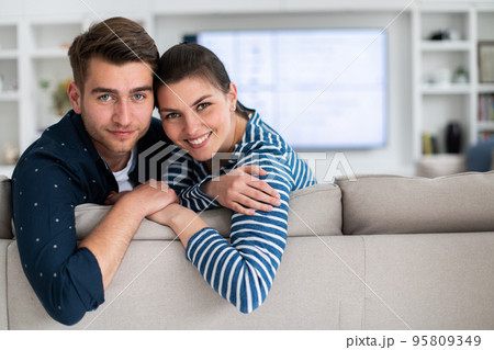 Couple Watches TV together while Sitting on a Couch in the Living Room. Girlfriend and Boyfriend embrace, cuddle, talk, smile and watch Television Streaming Services. Home with Cozy Stylish Interior. Couple Watches TV together while Sitting on a Couch in the Living Room. Girlfriend and Boyfriend embrace, cuddle, talk, smile and watch Television Streaming Services. Home with Cozy Stylish Interior. 95809349