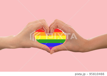 LGBT. Two females hands, shows the rainbow heart sign with their fingers. Copy space. Pink background. The concept of the LGBT movement and gay day 95810466