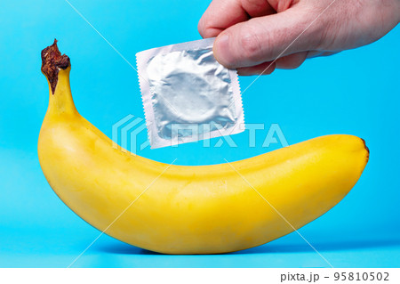 Yellow banana and a man's hand holding a package with a condom, on a blue background. The concept of safe sex 95810502