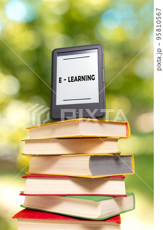 E-learning and reading. E-book reader is at the top of the stack of books. The Park is blurred in the background. Concept of education and electronic gadgets E-learning and reading. E-book reader is at the top of the stack of books. The Park is blurred in the background. Concept of education and electronic gadgets 95810567