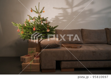 Small christmas tree with natural decorations and presents indoor near couch with warm light 95810697
