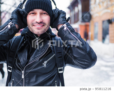 Close-up portrait of a smiling asian man listening to music via headphones during outdoor walking. 95811216