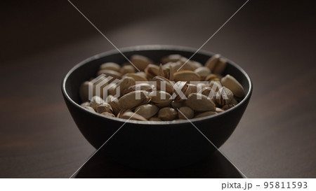 roasted pistachios in black bowl on walnut table 95811593
