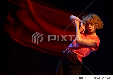 Art in motion. Portrait of young attractive girl with short curly red hair posing isolated over black background in mixed orange light. Art, beauty, fashion, trendy style Art in motion. Portrait of young attractive girl with short curly red hair posing isolated over black background in mixed orange light. Art, beauty, fashion, trendy style 95812758