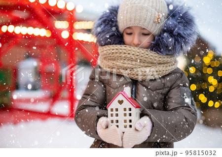 House, miniature cottage in hands of girl wearing mittens and warm clothes outdoor in snow. Family values, purchase housing, relocation, mortgage. Cozy home, Christmas, new year booking House, miniature cottage in hands of girl wearing mittens and warm clothes outdoor in snow. Family values, purchase housing, relocation, mortgage. Cozy home, Christmas, new year booking 95815032