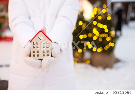 House, miniature cottage in hands of woman wearing mittens and warm clothes outdoor in snow. Deal for real estate, purchase, construction, relocation, mortgage. Cozy home, Christmas, new year booking House, miniature cottage in hands of woman wearing mittens and warm clothes outdoor in snow. Deal for real estate, purchase, construction, relocation, mortgage. Cozy home, Christmas, new year booking 95815066