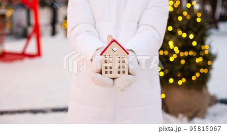 House, miniature cottage in hands of woman wearing mittens and warm clothes outdoor in snow. Deal for real estate, purchase, construction, relocation, mortgage. Cozy home, Christmas, new year booking House, miniature cottage in hands of woman wearing mittens and warm clothes outdoor in snow. Deal for real estate, purchase, construction, relocation, mortgage. Cozy home, Christmas, new year booking 95815067