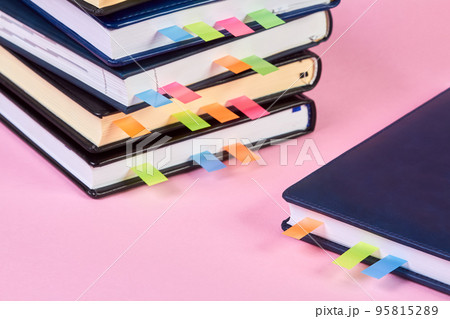 Close-up of a stack of office notepads with colorful sticky page markers sandwiched between pages on pink background 95815289