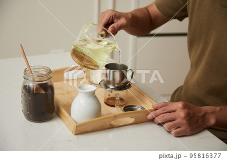 Hands of man pouring hot water in phin filter when making Vietnamese style coffee 95816377