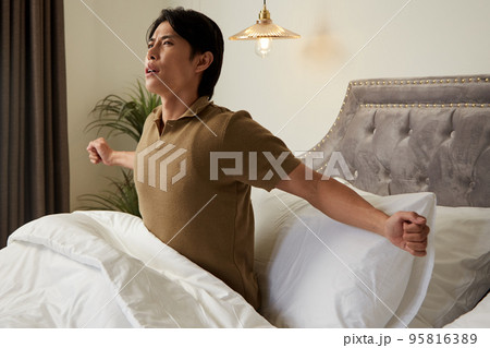 Young man stretching in bed after waking up in the morning Young man stretching in bed after waking up in the morning 95816389