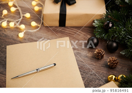 Blank sheet and pen on table with Christmas tree and wrapped present Blank sheet and pen on table with Christmas tree and wrapped present 95816491