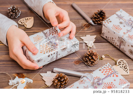 Gifts wrapped in festive paper in children's hands and Christmas decorations on a wooden background. Christmas preparations Gifts wrapped in festive paper in children's hands and Christmas decorations on a wooden background. Christmas preparations 95818233