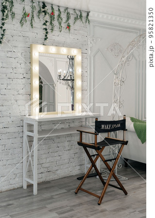 Table with makeup products and mirror near white wall, space for text. Dressing room interior 95821350