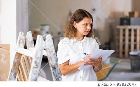 Woman with documents in her hands checks the quality of the completed repairs in cottage room 95822047