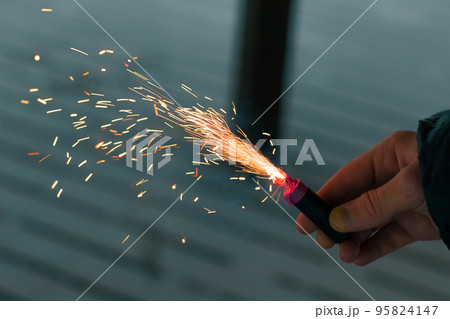 Burning Firecracker with Sparks. Guy Holding a Petard in a Hand 95824147
