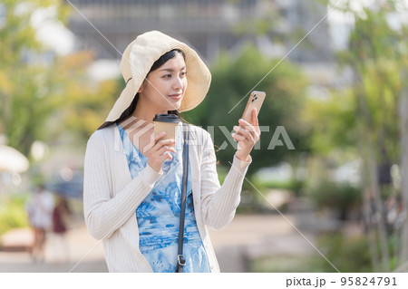 スマホと紙コップを持って街ブラを楽しむ若い女性 久屋大通公園にて 95824791
