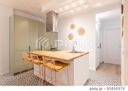 Bright warm kitchen with appliances, wooden island and high chairs in modern apartment 95830374