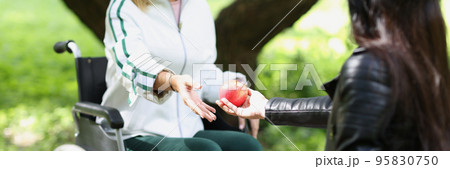 Woman passes apple to woman in wheelchair in park Woman passes apple to woman in wheelchair in park 95830750