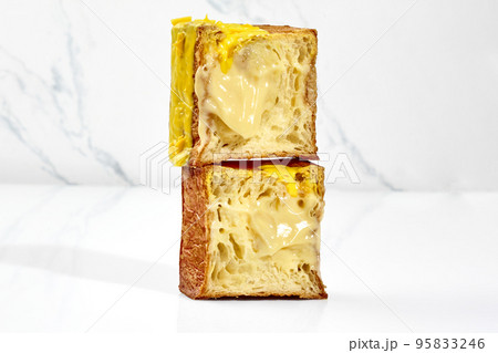 Sliced flaky cubic croissant with vanilla custard filling, yellow glaze and chocolate chips 95833246