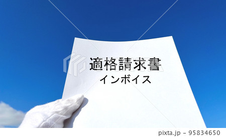 適格請求書文字入り白い紙を持つ白手袋の手_青空背景 95834650