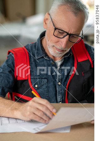 A bearded man sitting at the table and writing something 95837046