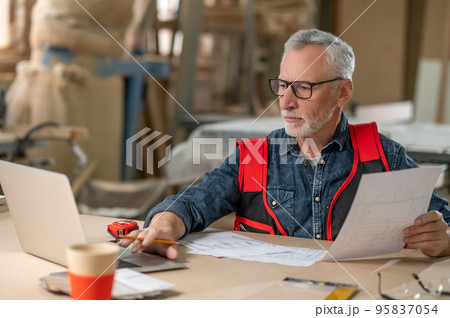 Mature man sitting at the laptop and checking papers 95837054