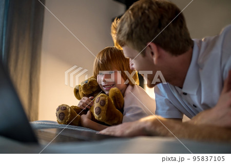 Father and son lying on bed and watching something on internet before going to sleep Father and son lying on bed and watching something on internet before going to sleep 95837105
