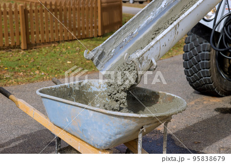 In construction site concrete mixer truck is pouring wet cement into wheelbarrow 95838679