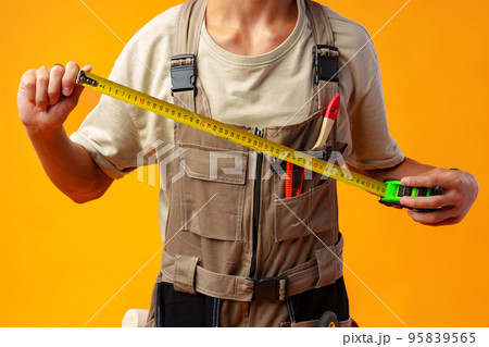 Close up of builder holding measuring roulette against yellow background in studio Close up of builder holding measuring roulette against yellow background in studio 95839565