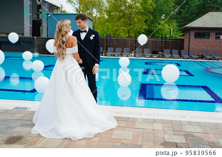 bride and groom in classic clothes by the pool decorated with white balloons.  95839566