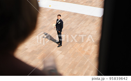 the groom with a bouquet of flowers is waiting for the bride on the window. 95839642