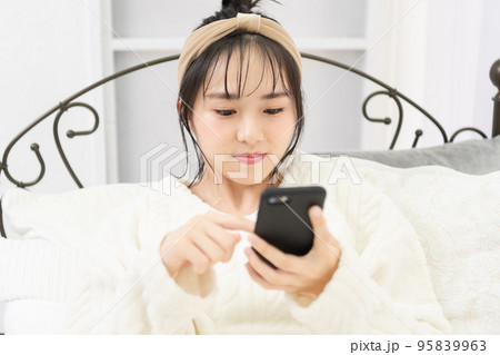 ベッドに寝転んでスマホを操作する若い女性 ベッドに寝転んでスマホを操作する若い女性 95839963
