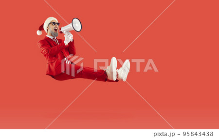 Happy man floating on red background, advertising Christmas sale and screaming through megaphone 95843438