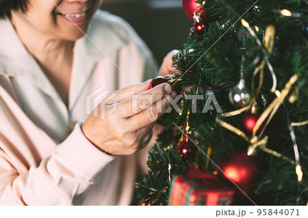 Close up elder woman hand decor Christmas tree at home. Close up elder woman hand decor Christmas tree at home. 95844071