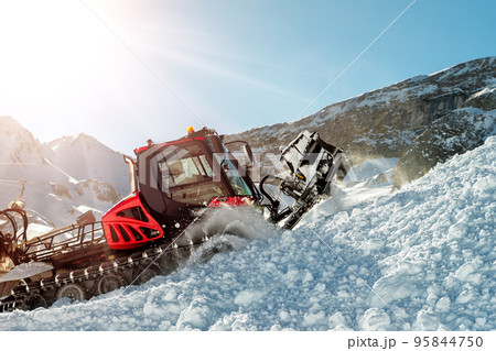 Red modern snowcat ratrack with snowplow snow grooming machine preparing ski slope piste hill at alpine skiing winter resort Ischgl in Austria. Heavy machinery mountain equipment track vehicle 95844750