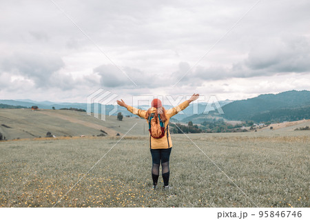 Hipster tourist woman with backpack and sleeping bag walks in the mountains in summer at sunset The girl travels to beautiful places. Mock up for text message. 95846746