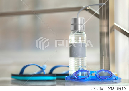 Swimming goggles, water bottle and flip flops against blurred background 95846950