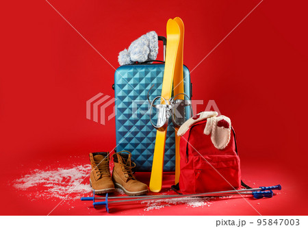 Suitcase with warm clothes and skis on red background. Winter vacation Suitcase with warm clothes and skis on red background. Winter vacation 95847003